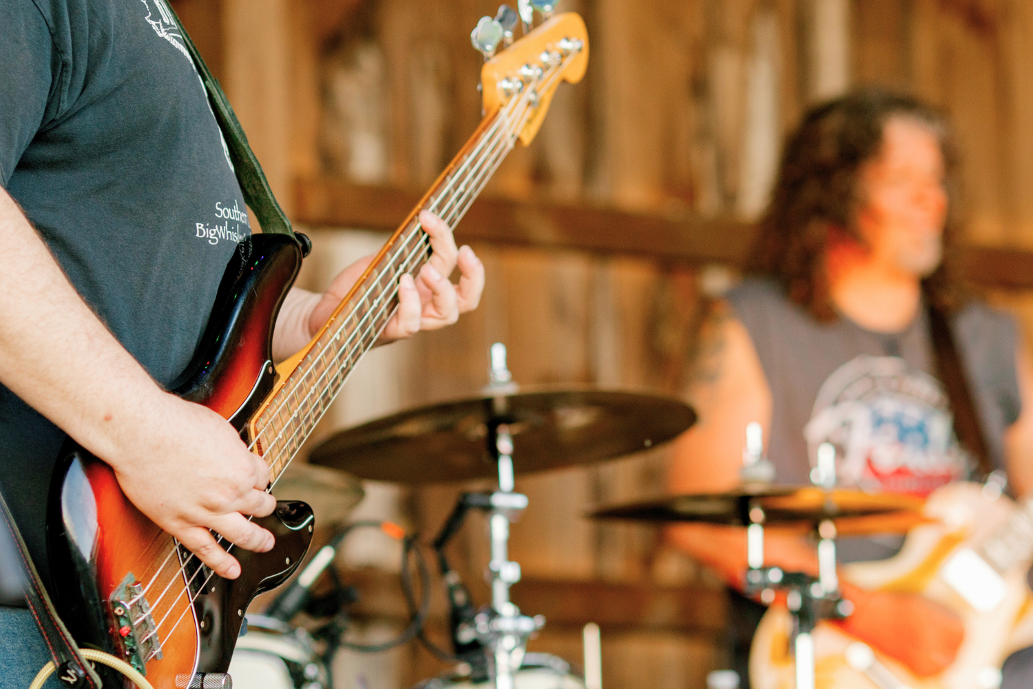 Two musicians playing guitar and drums in a wood-paneled room.