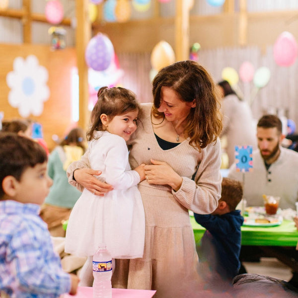 Woman holding a young girl in a festive indoor setting with balloons and decorations.