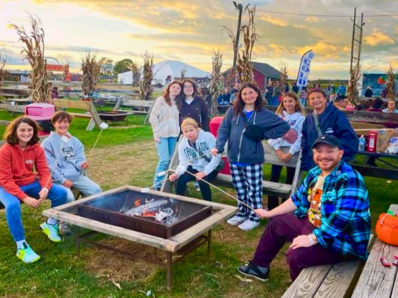 Group of people gathered around a fire pit at sunset in an outdoor setting.