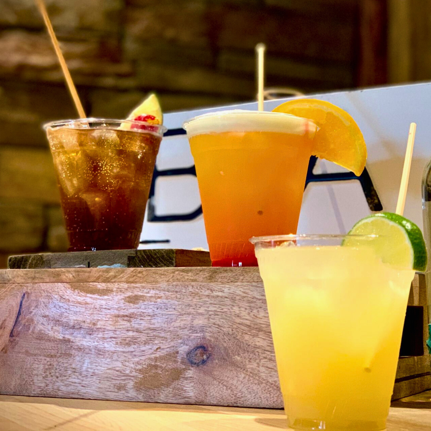 Three colorful cocktails with fruit garnishes on a wooden surface.